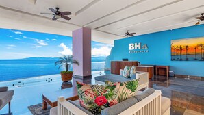 A spacious living area with a view of the ocean, a blue wall with the logo "BH Residences", and ceiling fans. - Blue Horizon 601 | 1BR/2BA Puerto Vallarta | Ocean Views, Pool, Gym (Puerto Vallarta)