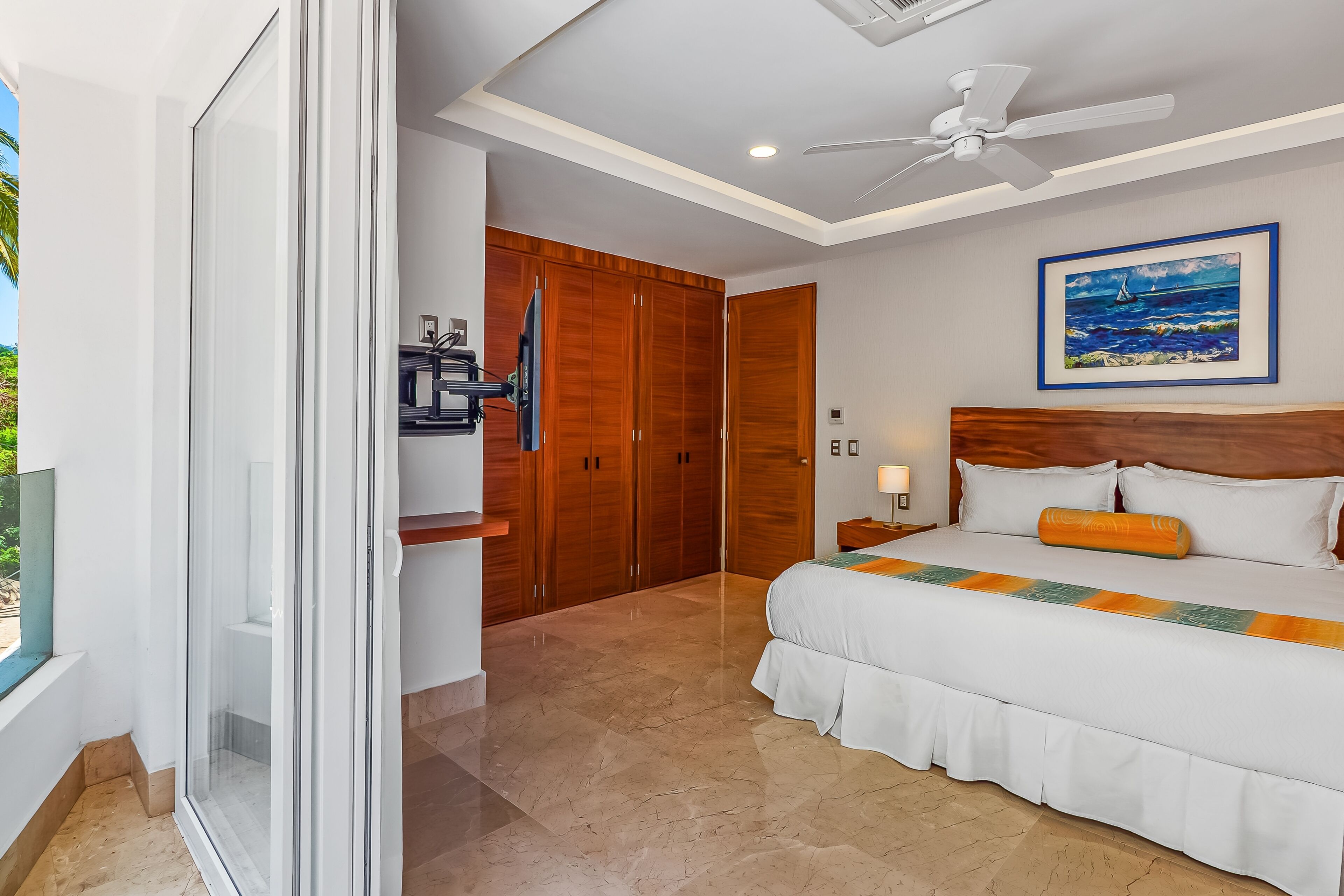 A bedroom with a large bed, wooden wardrobe, and a ceiling fan.