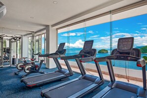 Ein Fitnessraum mit Laufbändern, Ergometer und Krafttrainingsgeräten mit Blick auf eine malerische Seelandschaft.