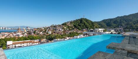 Uma piscina grande ao ar livre com vista para uma vila e montanhas ao fundo.