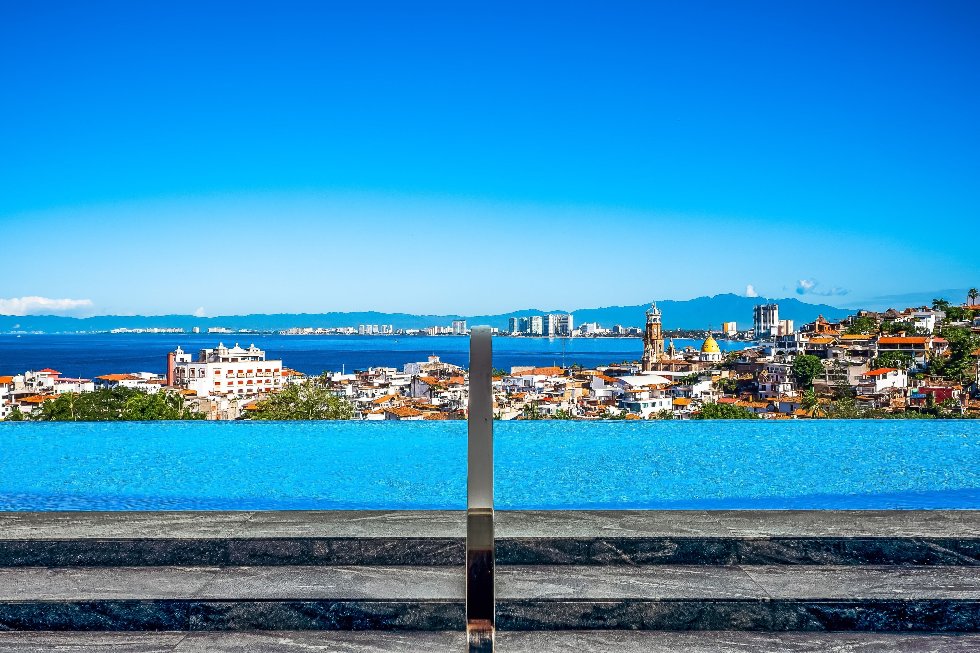 A cityscape with a prominent building in the foreground and a clear view of the coastline.