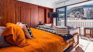 Ein modernes Schlafzimmer mit einem großen Bett, einem Flachbildfernseher und einem Balkon mit Blick auf die Stadt.