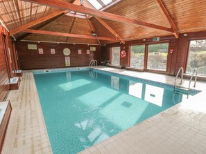 An indoor swimming pool with wooden beams, a lifeguard chair, and a view of the outdoors. - Cha Cha's Cottage, Near Whitby (Whitby)