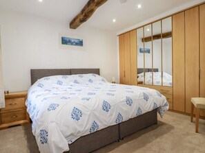 A bedroom with a bed, wooden wardrobe, and a mirror. - Harvenna Cottage, Crackington Haven (Bude)