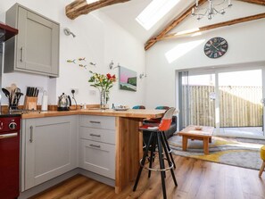 A kitchen with a wooden island, white cabinets, and a dining area with a table and chairs. - Harvenna Cottage, Crackington Haven (Bude)