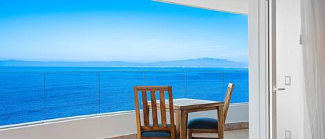 A balcony with a table and chairs, overlooking a body of water and distant mountains.