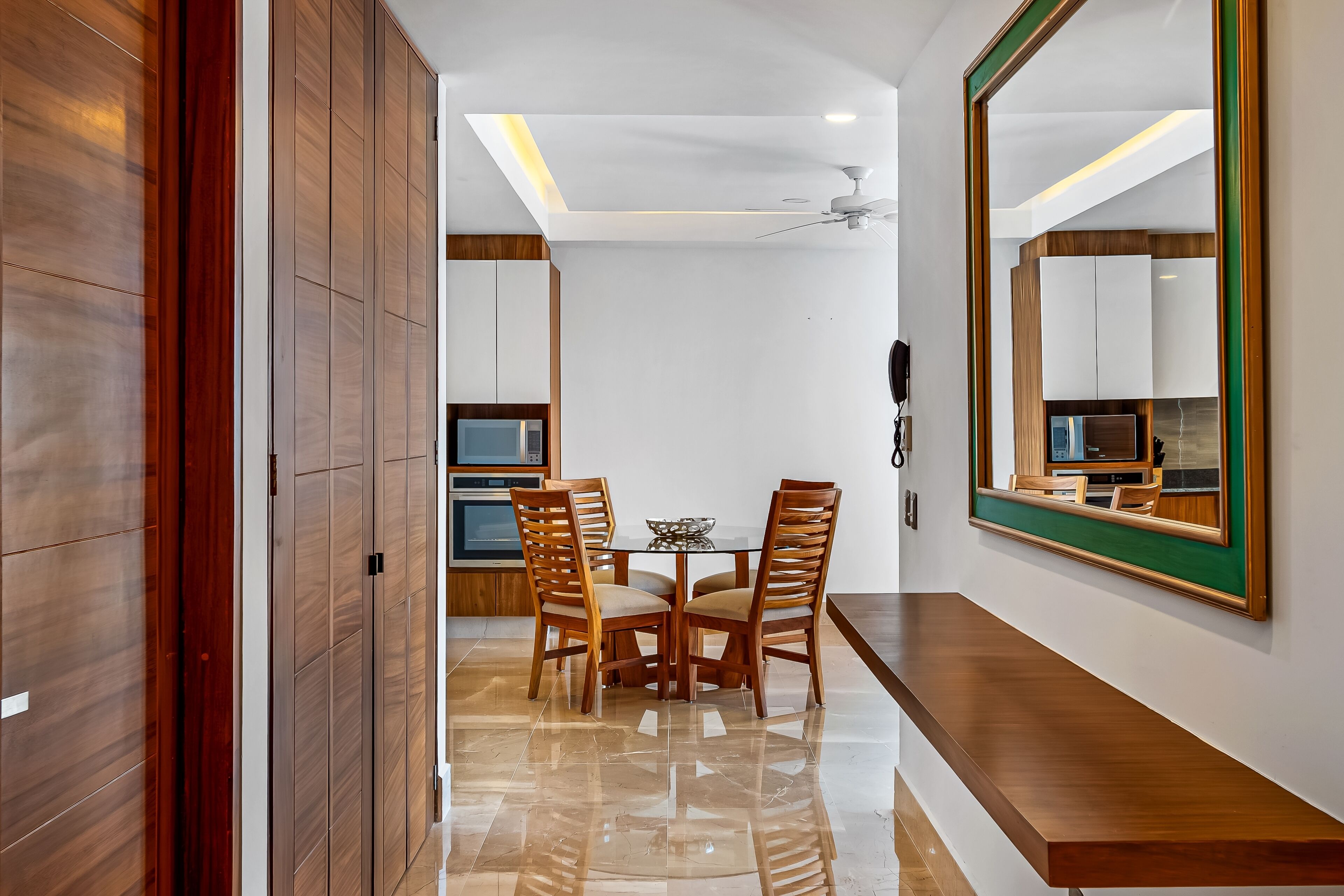 Un espace repas moderne avec une table et des chaises en bois, un ventilateur de plafond et un grand miroir au mur.