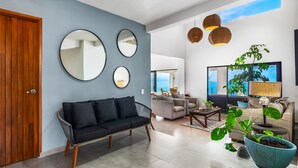 A modern living room with a black sofa, a large mirror, and a potted plant. - Ocean-view Conchas Chinas 3BR near beaches, dining, nightlife (Puerto Vallarta)