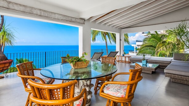 A glass-top dining table with wicker chairs, a sofa, and a view of the ocean. - Ocean-view Conchas Chinas 3BR near beaches, dining, nightlife (Puerto Vallarta)