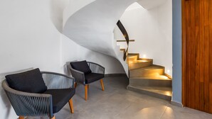 A modern interior with a curved staircase, two upholstered chairs, and a wooden door. - Ocean-view Conchas Chinas 3BR near beaches, dining, nightlife (Puerto Vallarta)