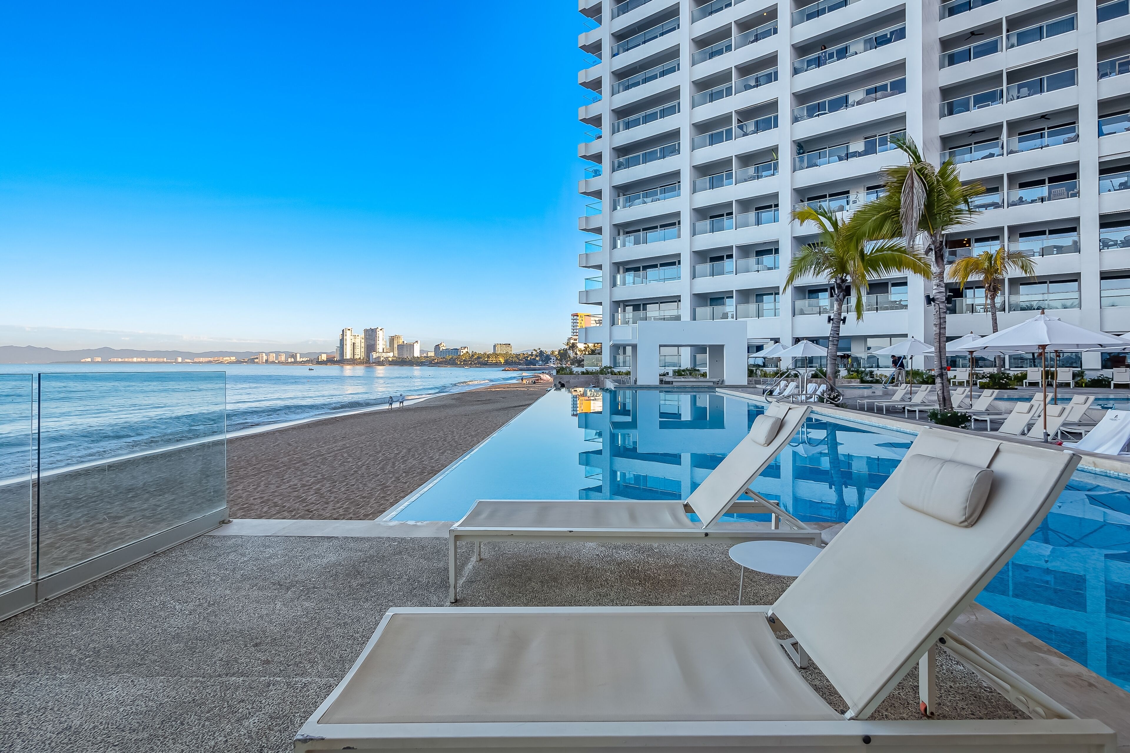 A poolside area with lounge chairs and a view of the beach and ocean.