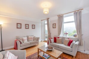 A living room with two sofas, a coffee table, and a floor lamp. There are curtains on the windows and framed pictures on the wall. - Swift Cottage, Pateley Bridge (Harrogate)