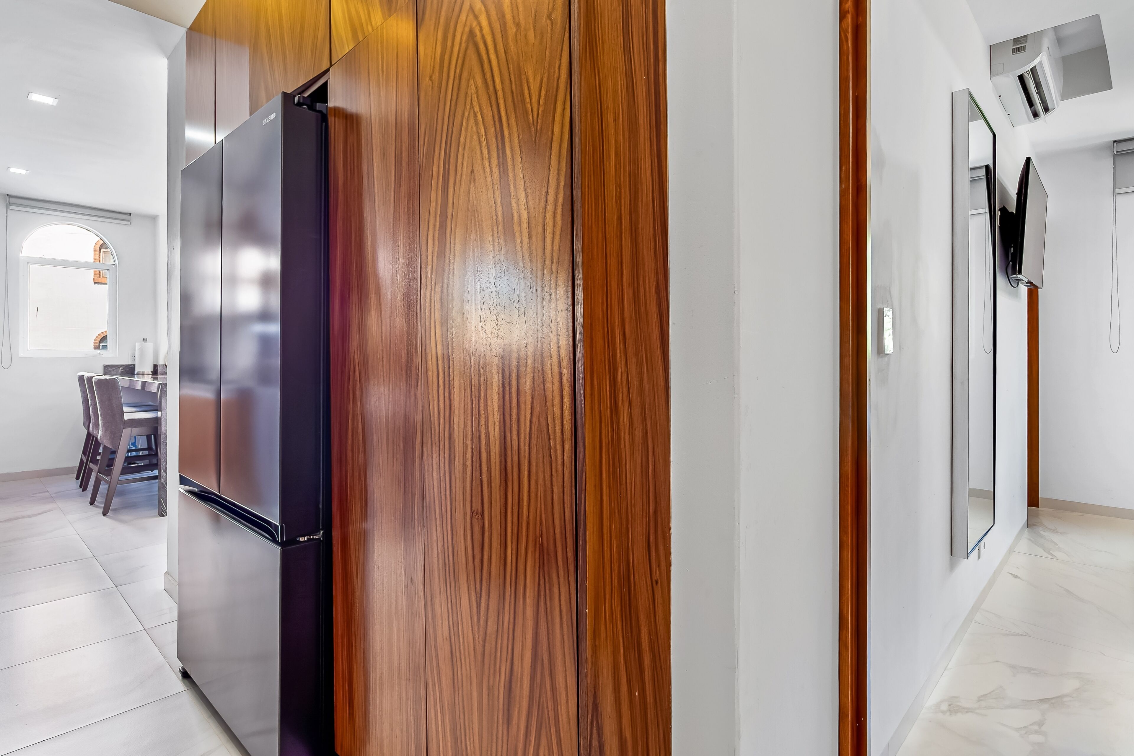 A modern kitchen with a stainless steel refrigerator, wooden paneling, and a marble floor.