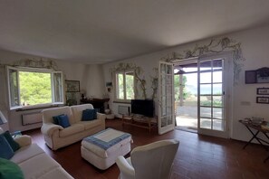 A living room with a sofa, ottoman, TV, and a sliding glass door leading outside.