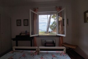 A room with a bed, a desk, a chair, a radiator, and a window with curtains.