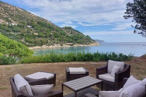 A coastal outdoor seating area with wicker furniture and a view of the sea.