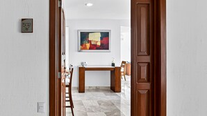 Un corridoio con una porta in legno, una scrivania e una sedia. Un quadro è appeso al muro.