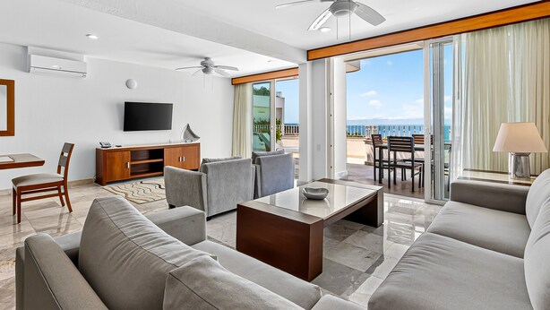 Una camera d'albergo moderna con un balcone, una TV a schermo piatto, un divano, un tavolino da caffè e un'area pranzo con vista sull'oceano.
