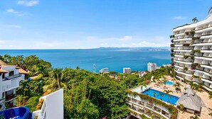 Un hotel sul lungomare con numerosi balconi, una piscina e vegetazione rigogliosa.