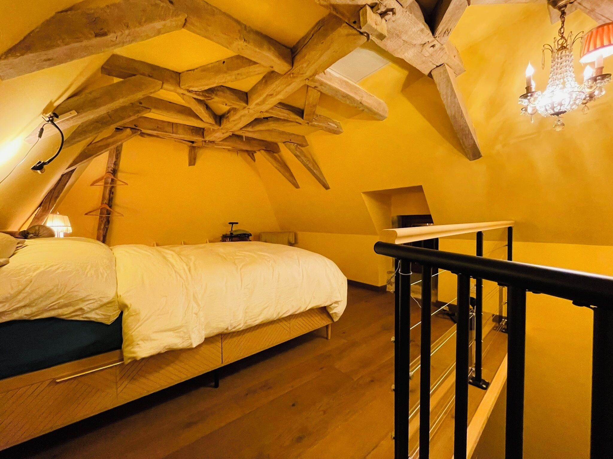 A bedroom with a wooden ceiling, a bed, a nightstand, a lamp, and a chandelier.