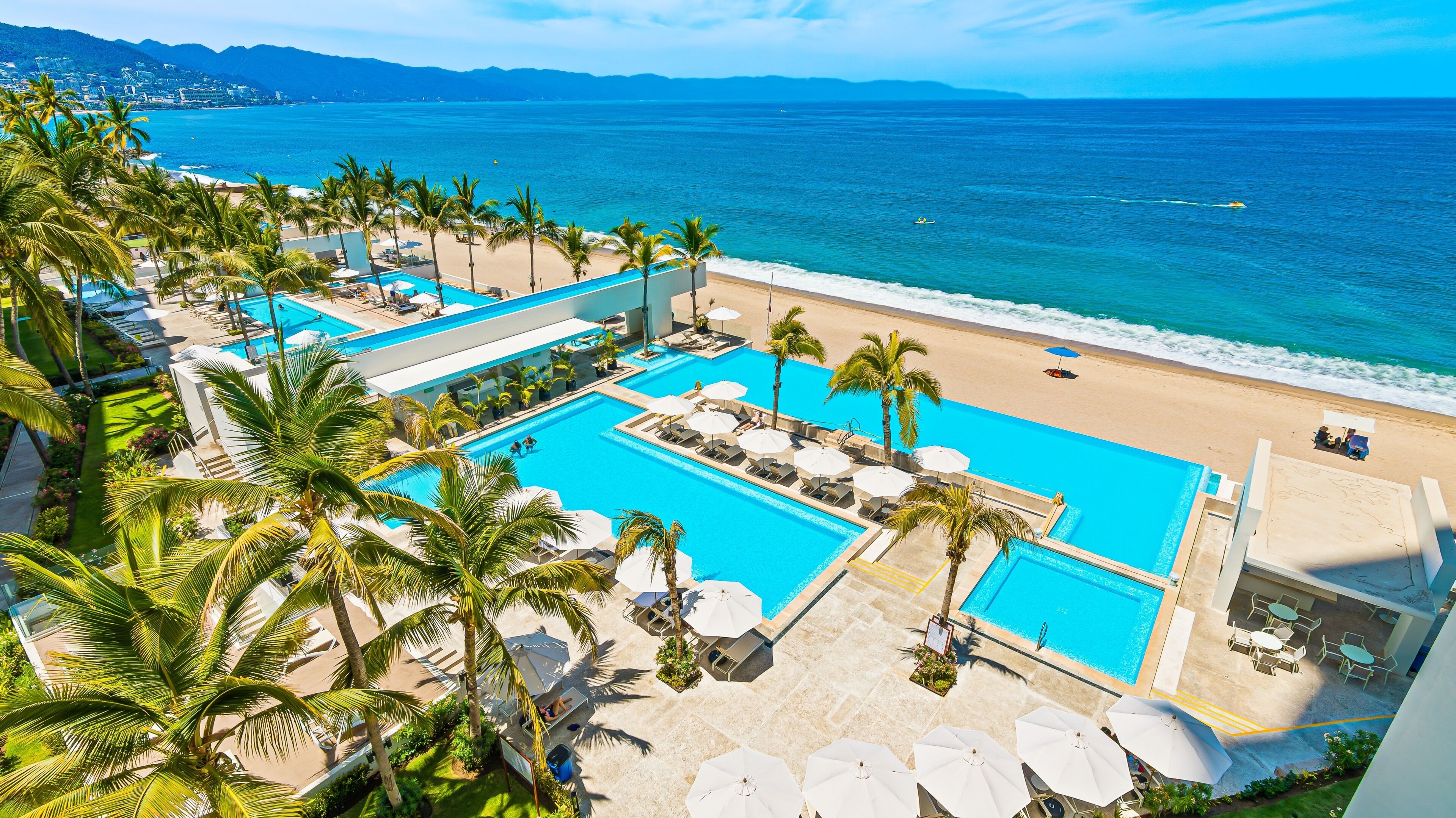 A resort with multiple swimming pools, a beach, and palm trees.