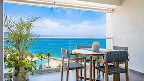 Ein Balkon mit Holztisch und -stühlen, einem Blumentopf und Blick auf das Meer.