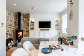 Ein gemütliches Wohnzimmer mit Steinwand, Kamin, Flachbildfernseher und Essbereich mit Tisch für zwei Personen.