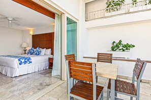 Ein Hotelzimmer mit Bett, Tisch und Stühlen. Es gibt einen Balkon mit Pflanzen und einer Brüstung.