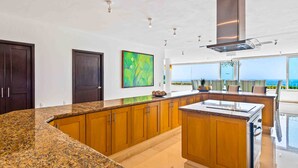 A modern kitchen with granite countertops, wooden cabinets, and a large island. - Elegant multi-level penthouse with rooftop Jacuzzi, bay views, pool & game room (Puerto Vallarta)