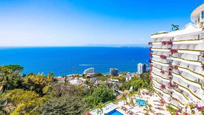 A coastal hotel with a pool, balconies with flowers, and a view of the sea. - Elegant multi-level penthouse with rooftop Jacuzzi, bay views, pool & game room (Puerto Vallarta)