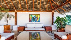 A covered outdoor seating area with wicker furniture, a large reflective table, and a colorful abstract painting on the wall. - Elegant multi-level penthouse with rooftop Jacuzzi, bay views, pool & game room (Puerto Vallarta)
