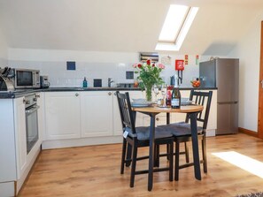A modern kitchen with white cabinets, a dining table with chairs, a microwave, a refrigerator, and a skylight.