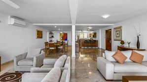 A spacious living area with a sofa, a dining table with chairs, and a kitchen in the background. - Elegant bayview suite with terrace access, full kitchen, pool, hot tub & gym (Puerto Vallarta)