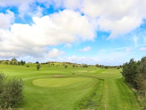 Ein Golfplatz mit blauem Himmel, sanften grünen Hügeln und vereinzelten Bäumen.