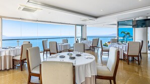 Un espace repas avec des tables rondes, des chaises et une grande fenêtre donnant sur la mer.