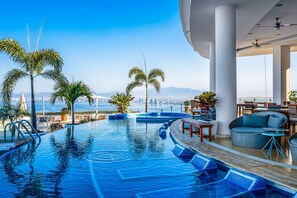 Zona de piscina con vistas al horizonte de una ciudad, palmeras y mobiliario exterior.