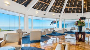 Un hall d’entrée spacieux avec un plafond haut, de grandes fenêtres donnant sur la mer et différents types de sièges.