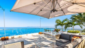 Une terrasse avec un canapé, une table basse et un parasol, offrant une vue sur la côte.