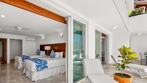 Moderni hotellihuone, jossa on suuri sänky, sohva, parveke, jossa on ruukussa oleva kasvi, ja kattotuuletin.