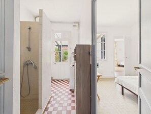 Ein Zimmer mit Schachbrettmuster-Boden, einem Bett, einer Holztür und einem Duschbereich.