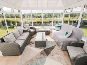 A sunroom with a large glass window, a grey sofa set, a white sofa set, and a coffee table.