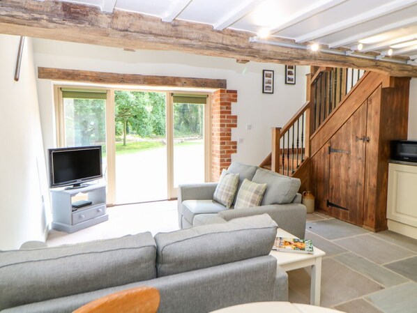 Una sala de estar con un sofá gris, televisor, escalera y vista al exterior.