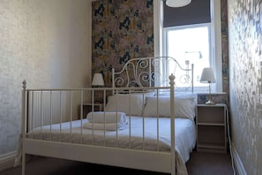 A bedroom with a white metal bed frame, a window with a view, and a floral wallpaper.