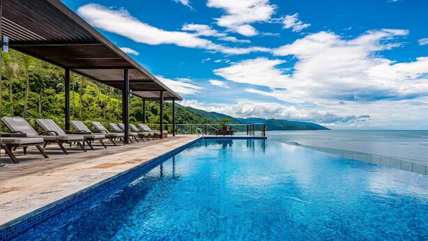 Uma piscina com espreguiçadeiras e área coberta, com vista para a água e vegetação.