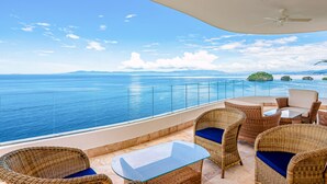 Varanda com móveis de vime e mesa de vidro com vista para o mar.