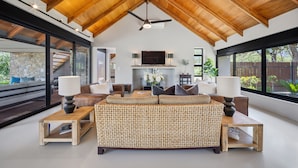 A spacious living room with a high ceiling, large windows, a fireplace, and a television. - Villa Nsovo (Hoedspruit)