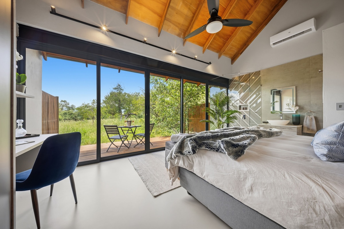 Quarto moderno com uma cama grande, uma escrivaninha e vista para o exterior.