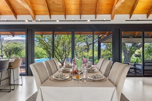 A dining area with a table set for six, large windows, and a view of the outdoors. - Villa Nsovo (Hoedspruit)