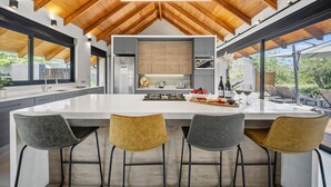A modern kitchen with a large island, bar stools, and a view of the outdoors. - Villa Nsovo (Hoedspruit)