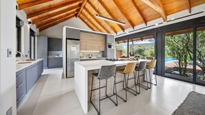 A modern kitchen with a large island, bar stools, and a view of the outdoors. - Villa Nsovo (Hoedspruit)